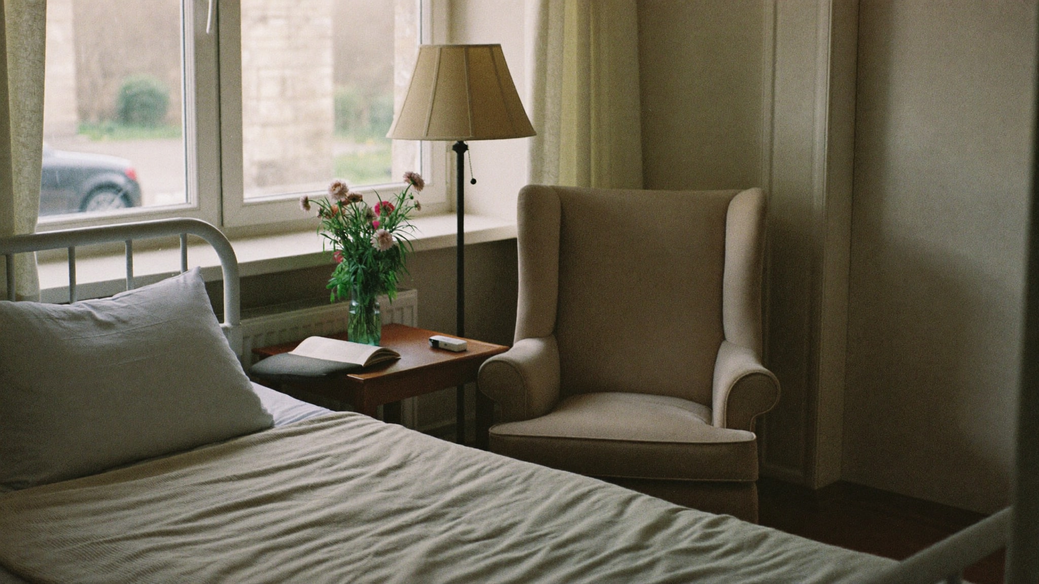 Ruhiges Hospizzimmer mit Bett, Besuchersessel und Blumen am Fenster