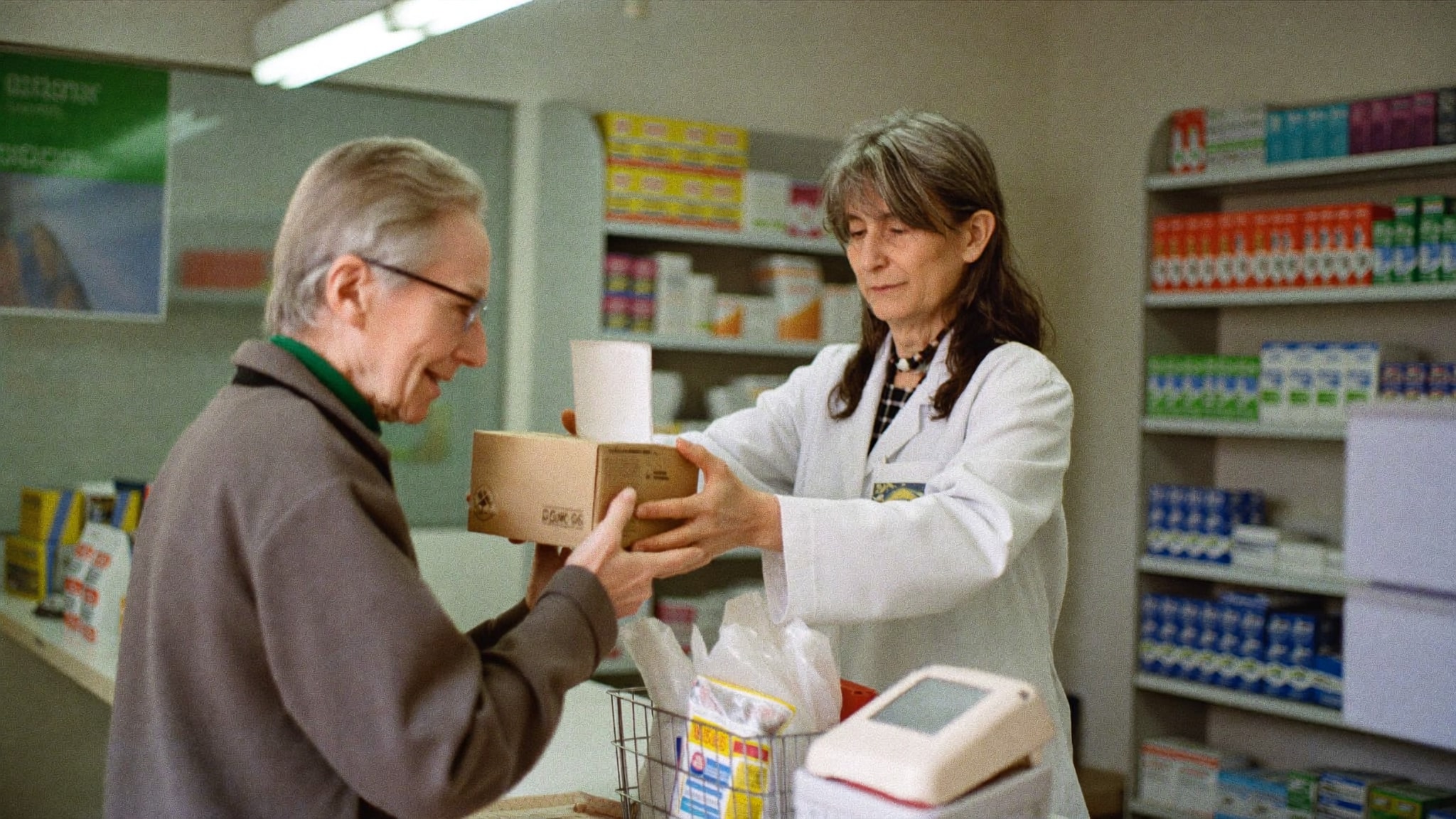 Apothekerin reicht einer älteren Kundin einen Karton mit Pflegehilfsmitteln über den Tresen