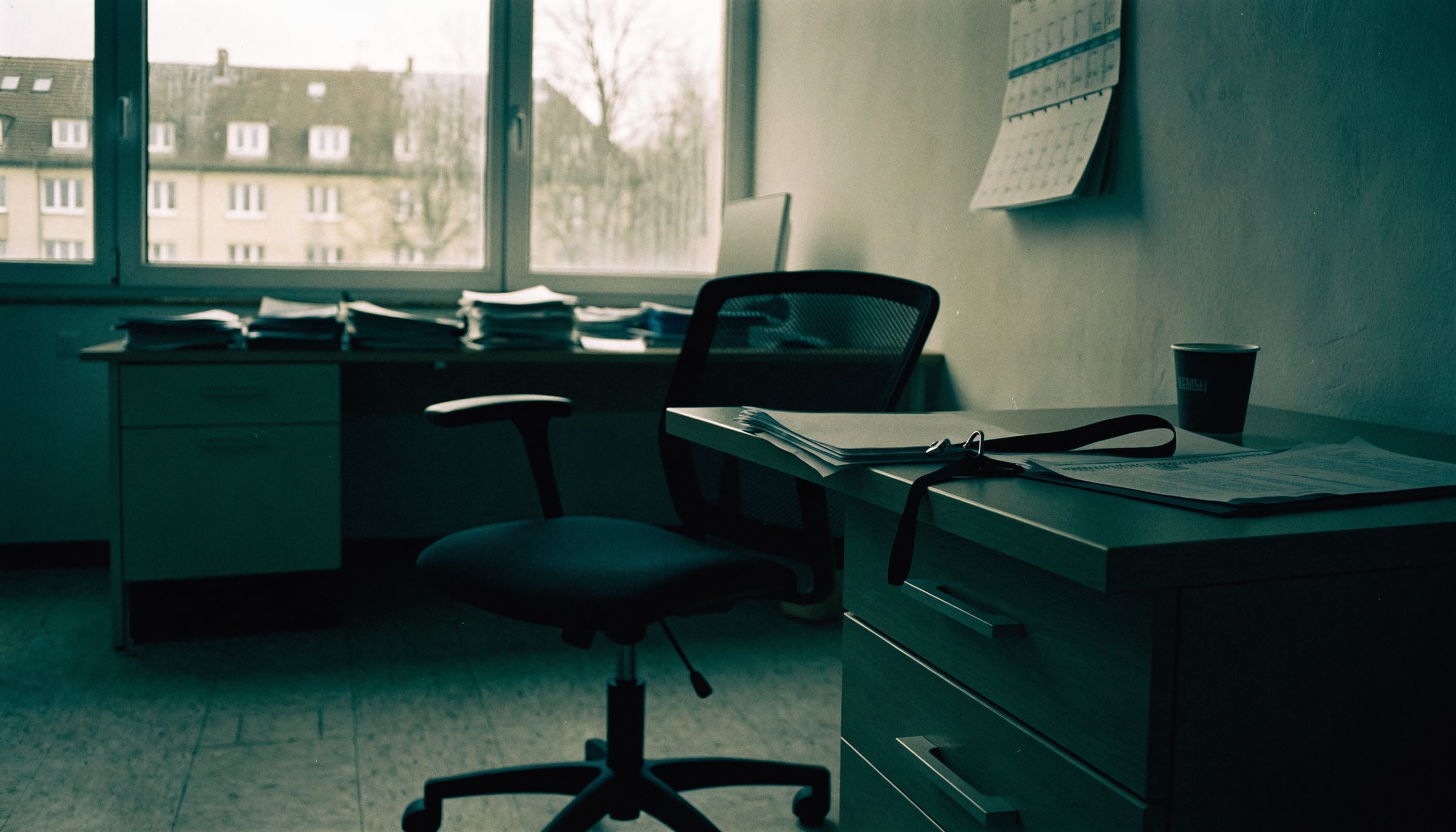 Leerer Bürostuhl vor einem Schreibtisch mit aufgeschlagenem Ordner, Schlüsselband und kalter Kaffeetasse im Büro eines ambulanten Pflegedienstes
